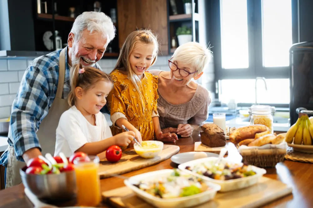 Foto de unos abuelos cocinando con sus nietos y sonriendo todos